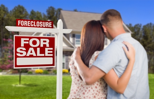 Military Couple in Front of House and Foreclosure For Sale Real Estate Sign.